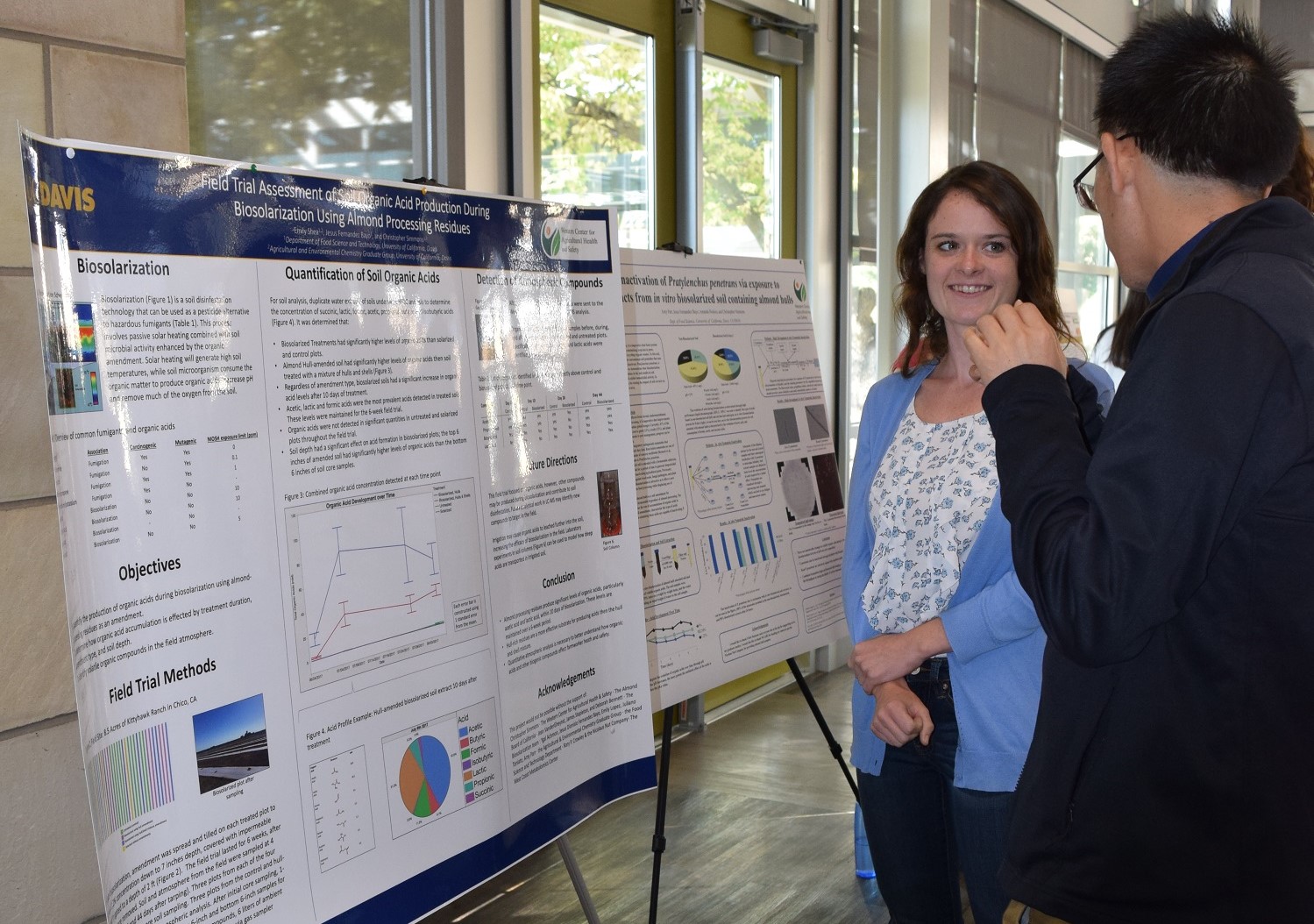 Emily Shea explains biosolarization poster to a man standing to her right