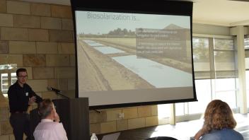 Dr Chris Simmons stands at podium in front of slide explaining biosolarization