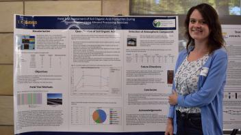 smiling woman stands next to poster with arms crossed