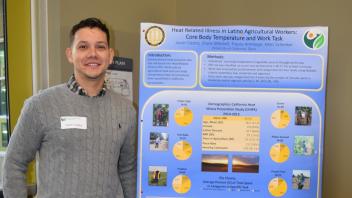 smiling man stands next to poster 