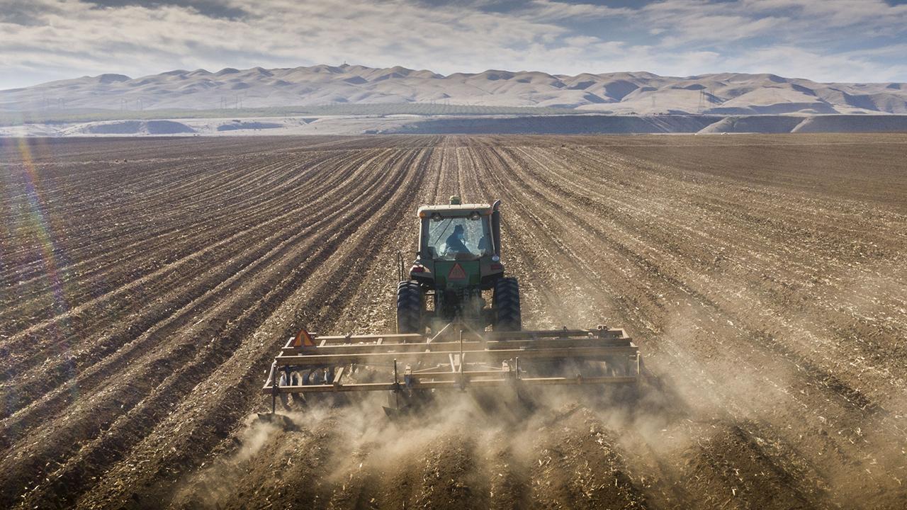 Tractor tills the soil and kicks up dust
