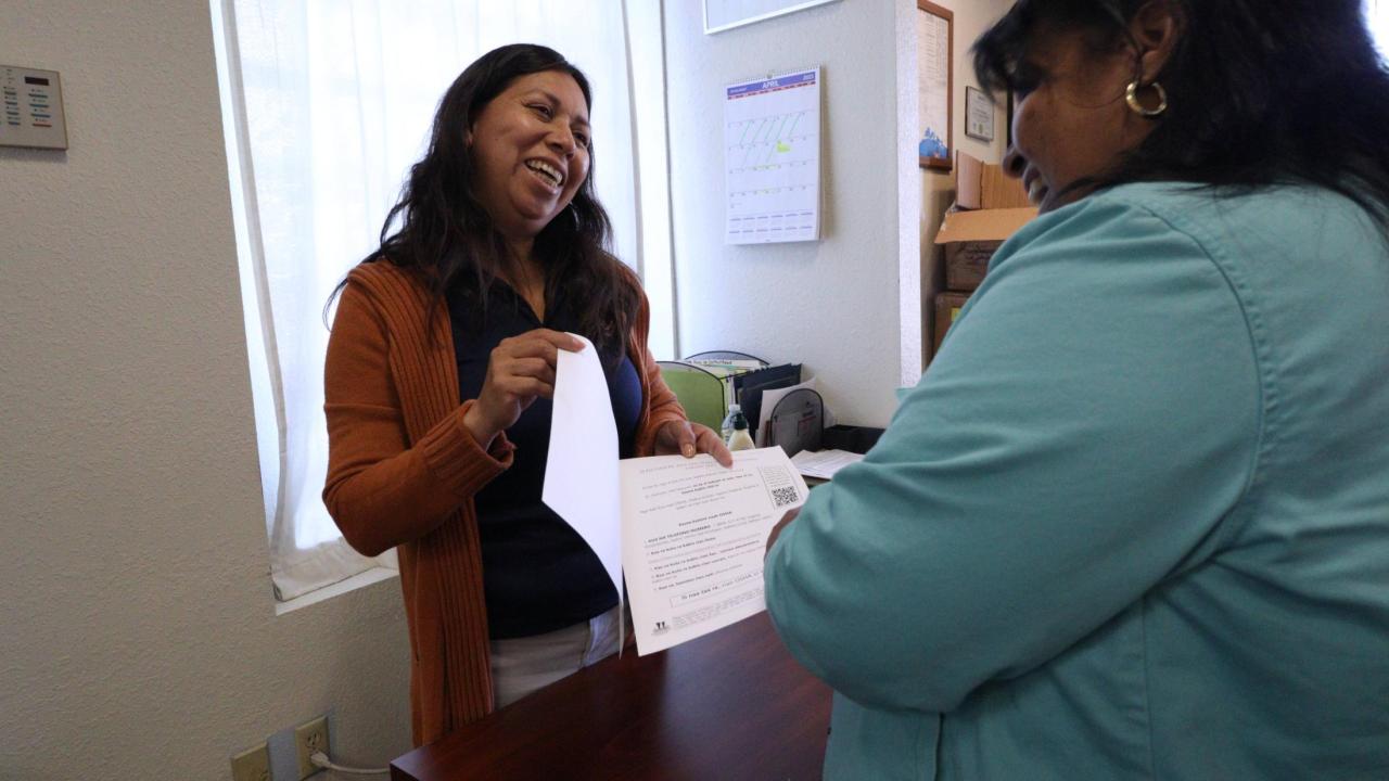 Woman in orange giving paperwork to woman wearing blue