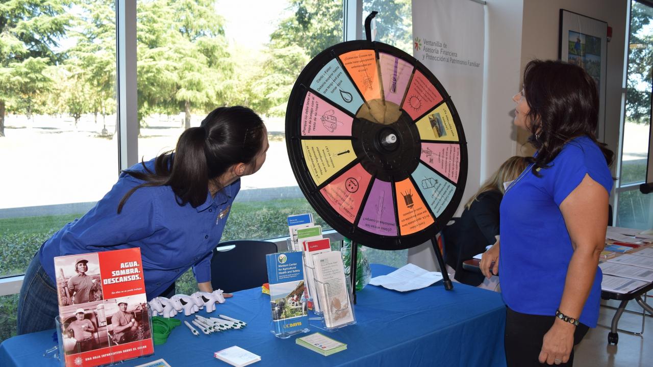 WCAHS Outreach worker play the spin the wheel game with a member of the public visiting the outreach table at an event