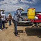 Farmworkers stand in line to get a drink of water from a cooler